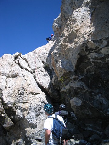 Jeff is standing at the bottom of a cliff looking up at Andrew who is already at the top.